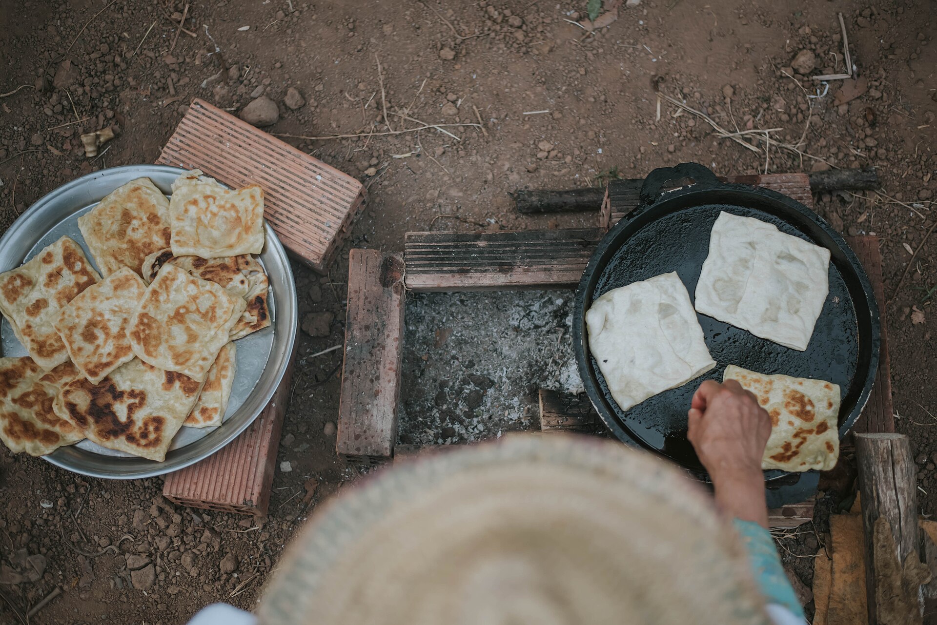 Moroccan flatbreads cooking on a griddle over an open fire, with finished breads on a tray
