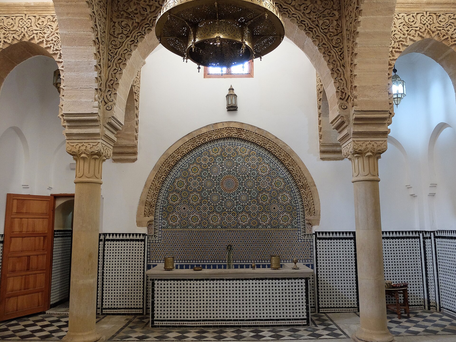 Interior of a traditional hammam with a zellige tile fountain and carved arches