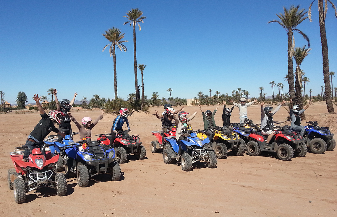 Group of riders on quad bikes with raised arms among palm trees under a blue sky